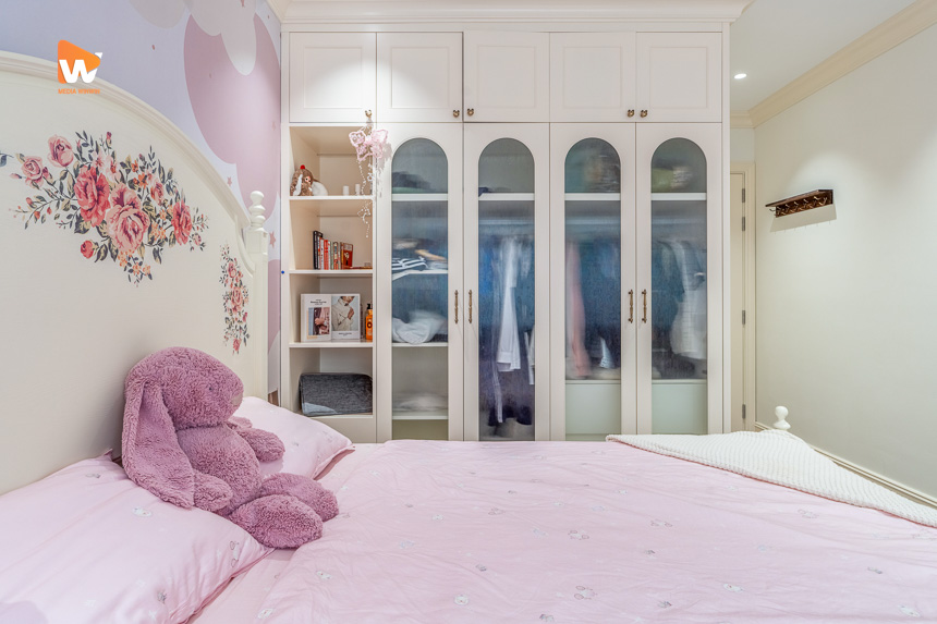 Phòng trẻ tông hồng đất với tranh hoa đầu giường và tủ cánh kính vòm